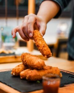 A person picking up a mozzarella stick from a large pile